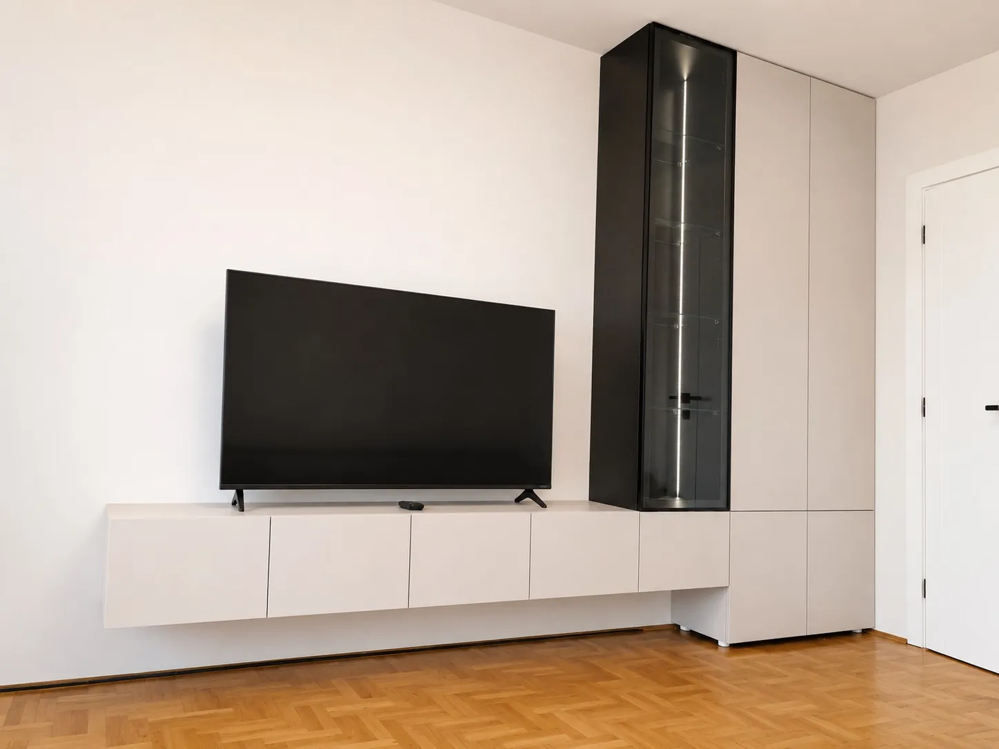 Lebdeća TV komoda u beloj sa crnom vitrinom sa staklenim vratima u dnevnoj sobi